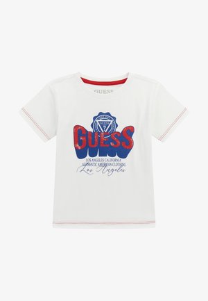 T-shirt in cotone bianco con un logo "GUESS" rosso e blu di grande dimensione con design a distintivo. Include cuciture decorative rosse sulle maniche.