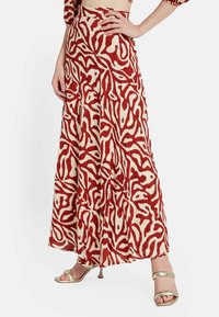 Falda larga y fluida en crema con un patrón abstracto en rojo, con una cintura alta y movimiento. Combinada con tacones metálicos con tiras.