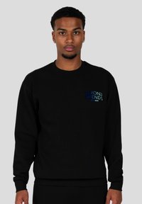 Sudadera negra con cuello redondo, mangas largas y puños de canalé. Presenta un colorido logo "WRONG FRIENDS" bordado en el pecho.