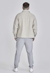 Light gray wool-blend shirt jacket with a collar and button cuffs, paired with light gray sweatpants, finished with white sneakers.