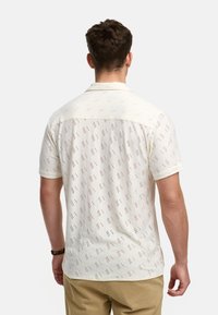 Camicia a maniche corte in tessuto crema chiaro con un motivo a onde, caratterizzata da piccoli accenti rossi e neri. Collo classico e chiusura a bottoni.
