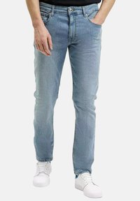 Jasnoniebieskie jeansy o slim fit, z pięcioma kieszeniami, subtelnym przetarciem i widocznymi szwami. Połączone z białymi trampkami.