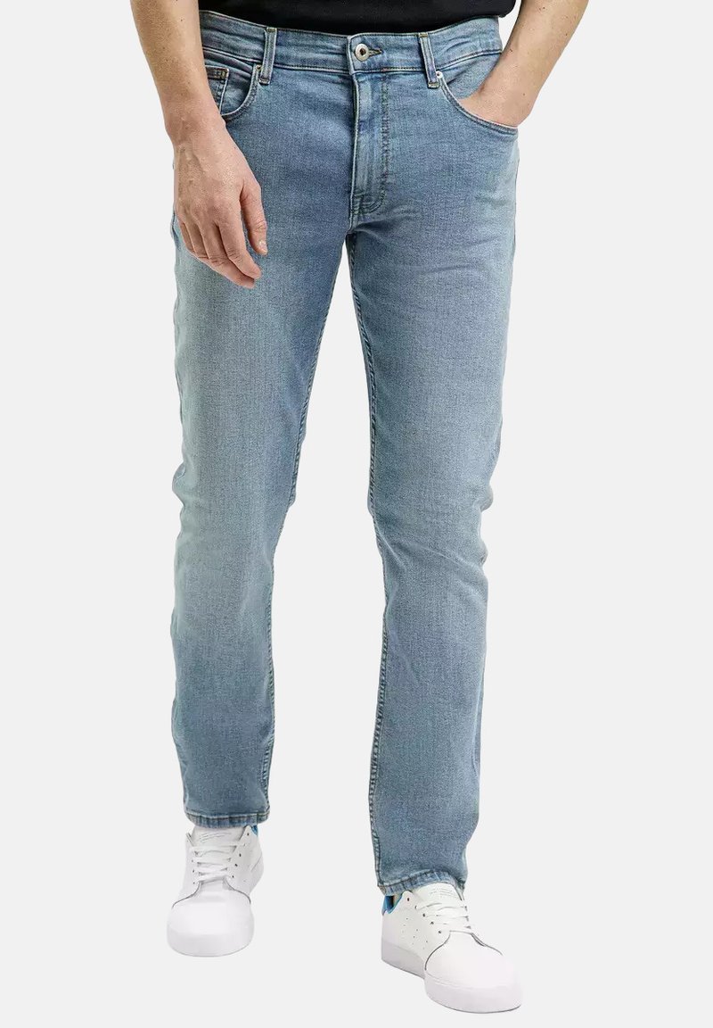 Jasnoniebieskie jeansy o slim fit, z pięcioma kieszeniami, subtelnym przetarciem i widocznymi szwami. Połączone z białymi trampkami.