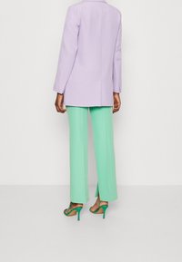 Blazer lilas ajusté, associé à un pantalon vert menthe à jambes larges avec des fentes latérales, et des sandales vertes à talons hauts avec des lanières.