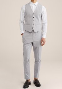 Ljusgrå skräddarsydd kostym i tre delar med väst, slim fit-byxor och en vit skjorta. Inkluderar svarta loafers. Slät tygtextur.