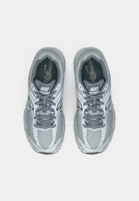 Par de zapatos de correr Nike grises y blancos con parte superior de malla y material sintético, etiquetados como "MOTO 2K", vistos desde arriba sobre un fondo blanco.