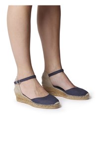 Espadrillas con zeppa in tela blu navy, sole in corda di juta e cinturino alla caviglia, con punta arrotondata e lati aperti per una migliore traspirabilità.