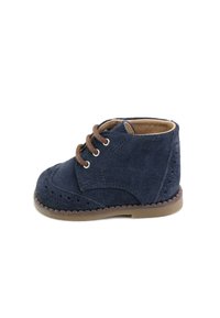 Zapato de ante azul marino con cordones y detalles de brogue, con suela cosida en color marrón claro y cordones marrones, que presenta una puntera redonda y altura hasta el tobillo.