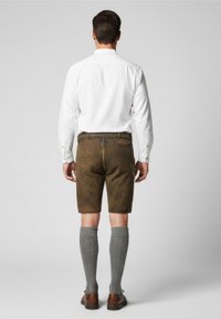 Bruine leren shorts gecombineerd met een wit knoopshirt, grijze kniehoge sokken en bruine schoenen, gezien vanaf de achterkant.