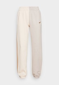 Nike joggingbroeken in beige en lichtbruin, gemaakt van zachte stof. Beschikt over een drawstring taille, elastische boorden en een subtiele logo-accent.