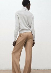 Maglione grigio chiaro a collo alto abbinato a pantaloni larghi color beige, entrambi caratterizzati da una texture morbida e una vestibilità sartoriale. Design semplice e moderno.