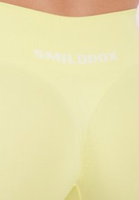 Geel geribde leggings met een hoge tailleband. De tekst "SMILODOX" in het wit gedrukt. Soepele textuur, nauwsluitend ontwerp zonder zichtbare patronen of accenten.