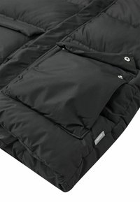 Schwarzer gepolsterter Jackenärmel mit einer Druckknopfklappen-Tasche und einem kleinen grauen Stoffmarkenetikett, das nahe dem Bündchen genäht ist.