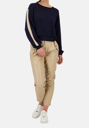 Marineblaues Sweatshirt mit beigen Streifen an den Ärmeln, kombiniert mit beigen Kunstlederhosen mit Druckknopf-Taschen und weißen Sneakern.