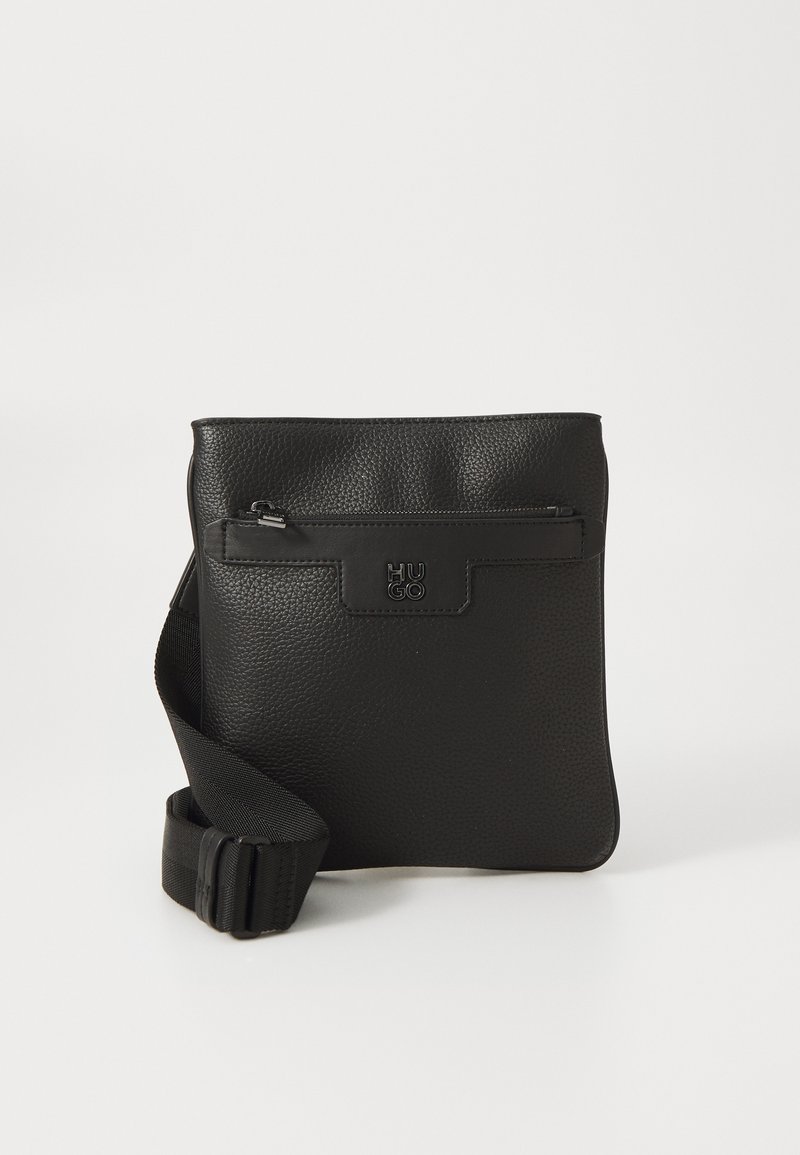 Črna usnjena torbica čez ramo z teksturirano površino, sprednji žep na zadrgo, nastavljiv pas in embosiran logotip. Pravokotna oblika.