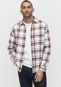 Rutet flannel skjorte i hvid, rød og marineblå. Lange ærmer, knaplukning foran, brystlomme, og en afslappet pasform. Båret over en hvid t-shirt.