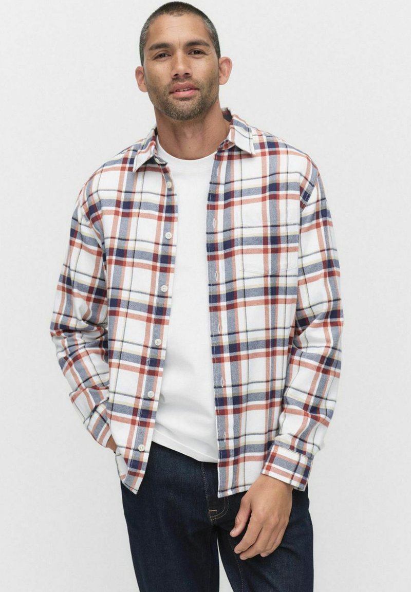 Rutet flannel skjorte i hvid, rød og marineblå. Lange ærmer, knaplukning foran, brystlomme, og en afslappet pasform. Båret over en hvid t-shirt.