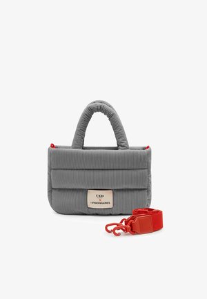 Sac à main matelassé gris avec poignées courtes rembourrées, une étiquette à l'avant et une bandoulière rouge amovible avec des attaches à côté.