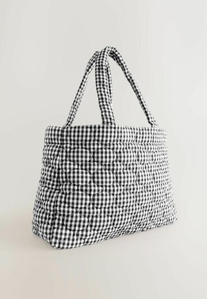 Svart och vit rutigt quiltad tote-väska med cirkulärt vadderat mönster och två vadderade handtag på en neutral bakgrund.