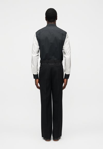 Černobílá bunda s propracovaným designem, která má černý zadní díl a bílé rukávy, doplněná černými na míru šitými kalhotami.