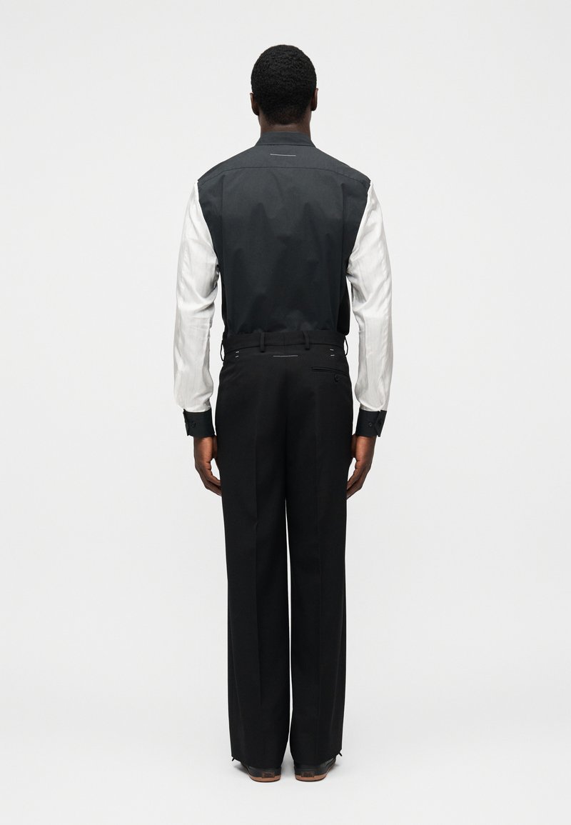 Veste noir et blanc au design structuré, avec un dos noir et des manches blanches, associée à un pantalon noir ajusté.