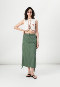 Witte cropped top met rode geometrische borduursels, gecombineerd met een olijfgroene maxi rok met een elastische taille en een zijzak.