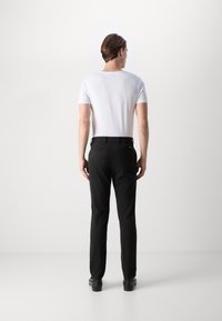 T-shirt bianco a maniche corte abbinato a pantaloni neri. I pantaloni presentano passanti per cintura e tasche posteriori, creando una silhouette pulita e slanciata.