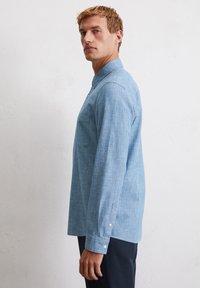 Chemise boutonnée bleu clair en mélange de lin, dotée d'un col classique, de manches longues, d'une poche poitrine unique et d'une texture subtile.