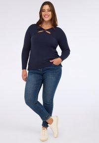 Pulover tricotat cu nervuri de culoare bleumarin, cu un detaliu în formă de cheie, asortat cu blugi albaștri cu accente cu ținte la manșete și adidași albi.