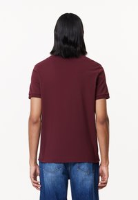 Burgundy kortärmad t-shirt med rund hals, tillverkad av mjukt tyg, har en enkel design och är tillsammans med blå denimjeans.