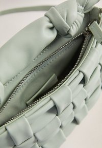 Sac à main en cuir vert menthe avec un design tissé, doté d'une poignée nouée, d'une poche zippée et d'une texture lisse. L'intérieur est doublé.