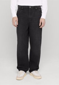 Mustad sirge lõikega teksapüksid, millel on kõrge vöökoht, viis taskut ja ees nööpkinnitusega sulgumine. kantud valgete tossudega.