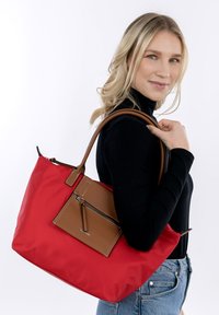 Red nylon tote bag with brown leather accents and a front zip pocket. Features sturdy dual handles and a simple, functional design.