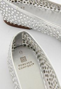 Sølvflade sko med en tekstureret overflade, der har klare pyntdetaljer, en glat inderside og en mærket indersål. Størrelsen er angivet som 6½.