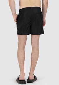 Shorts de bain noirs avec une taille élastique et une seule poche au dos. Fabriqués en matériau léger et à séchage rapide, avec une texture lisse.