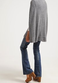 Grå stickad cardigan med lös passform, ihopparad med blå utsvängda jeans och bruna klackskor med tjock tå. Texturen synlig i tröjans material.