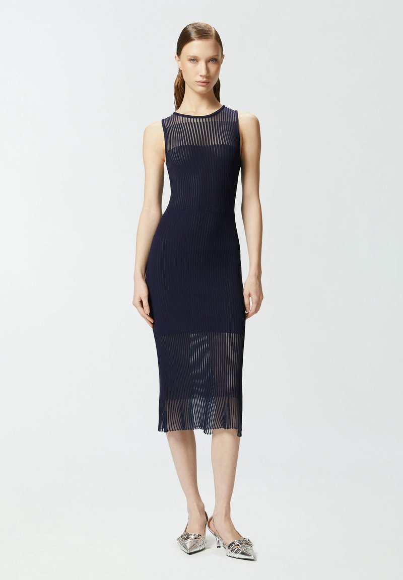 Morska plava rebrasta midi haljina s prozirnim dijelom na izrezu i lepršavim rubom. Uparena sa srebrnim cipelama na petu. Glatka tekstura.