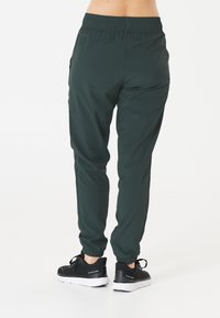 Mörkgröna sportbyxor med elastisk midja och muddar, tillverkade av ett slätt, lätt tyg. Kombineras med svarta sneakers.