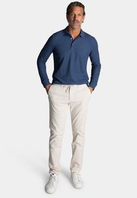 Polo-shirt met lange mouwen in marineblauw met knoopjeskraag, gecombineerd met lichtbeige joggerbroeken en witte sneakers. Bevat een rode logodetail.