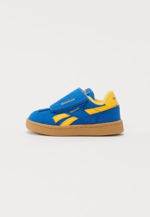 Baskets Reebok pour tout-petit bleu et jaune avec bande Velcro et semelle marron, présentées en profil latéral sur un fond blanc.