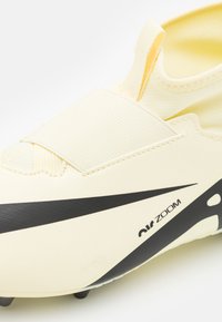 Botas de fútbol amarillas con un diseño elegante, parte superior texturizada, logo de Nike en negro y correa elástica en la parte frontal para mayor soporte.