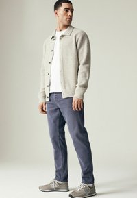 Cardigan en mélange de laine gris clair avec une texture côtelée, fermeture à boutons, t-shirt blanc à col rond, jean bleu foncé et baskets grises.
