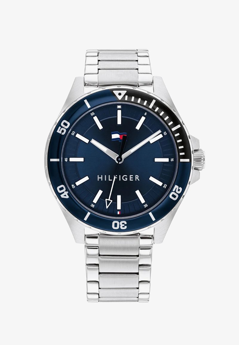 Hõbedane metallkell roostevabast terasest rihmaga, tume sinine kellaseier, valged tunni näidikud ja must ääre. Omab brändi nime "HILFIGER."