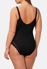 Svart spetsbodysuit med djup rygg, justerbara band och scallop-edgar på benöppningarna, som visar blommönster genom hela.