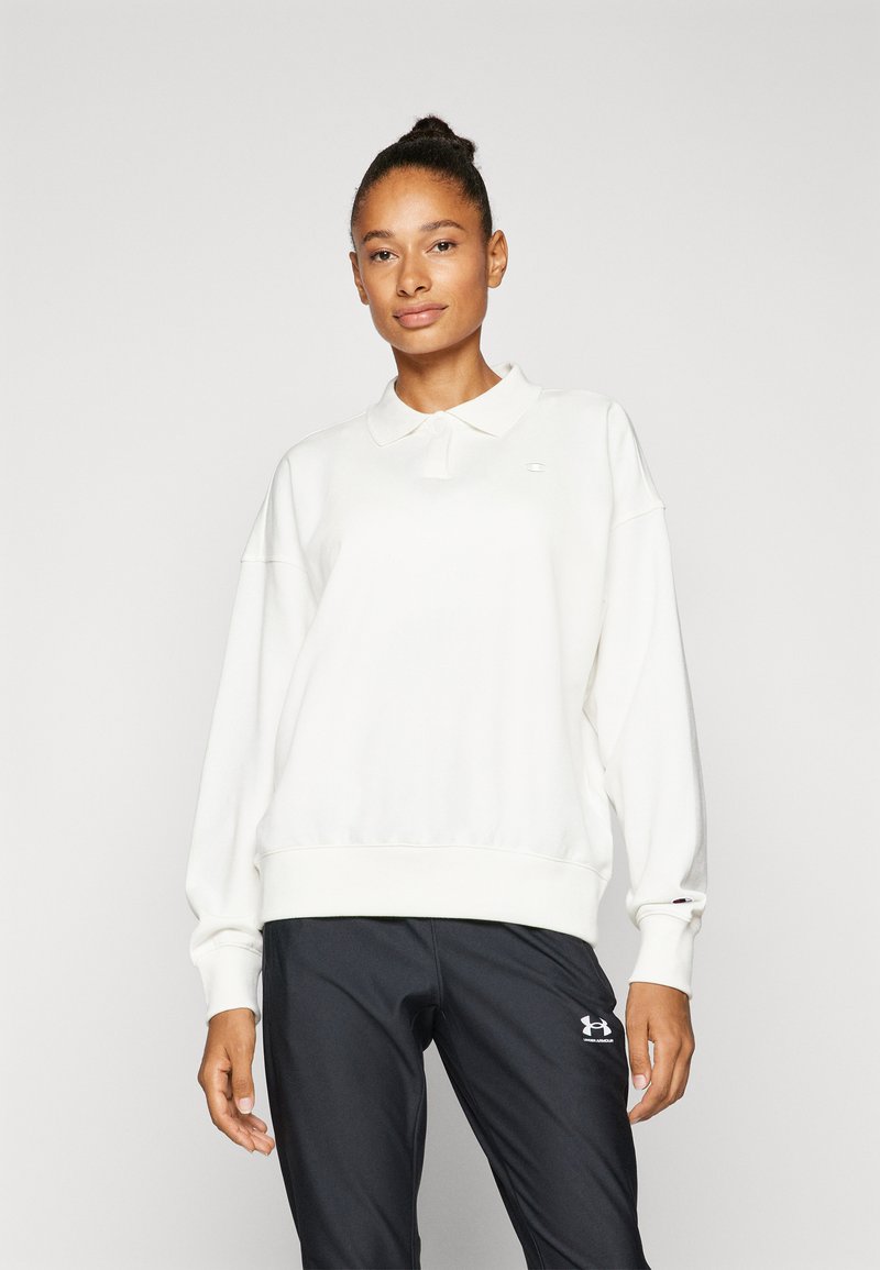 Felpa polo bianca a maniche lunghe con polsini e orlo a coste, dotata di un piccolo logo sul lato sinistro del petto. Abbinata a pantaloni sportivi neri.