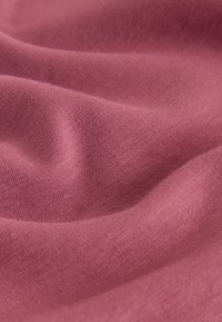 Tessuto rosa morbido e liscio con una texture a maglia fine visibile e pieghe delicate che creano morbide ombre e luci.