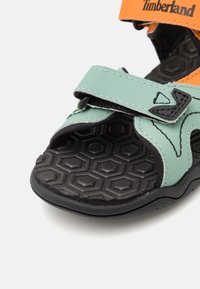 Grønn og oransje sandal med justerbare borrelåsremmer, teksturert svart sekssidet såle og forsterkede sømmer.