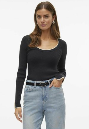 Top lungo a maniche nere a coste con scollo rotondo, con dettagli crema sul colletto e sui bordi delle maniche, abbinato a jeans azzurri chiari e una cintura nera.