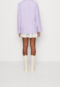 Lila oversized blazer med långa ärmar, kombinerad med en blommig minikjol och knähöga kremfärgade stövlar. Slätt tyg och avslappnad passform.