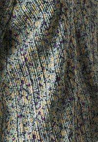 Primer plano de una tela plisada con un pequeño patrón floral en amarillo, púrpura, negro y blanco sobre un fondo verde claro.